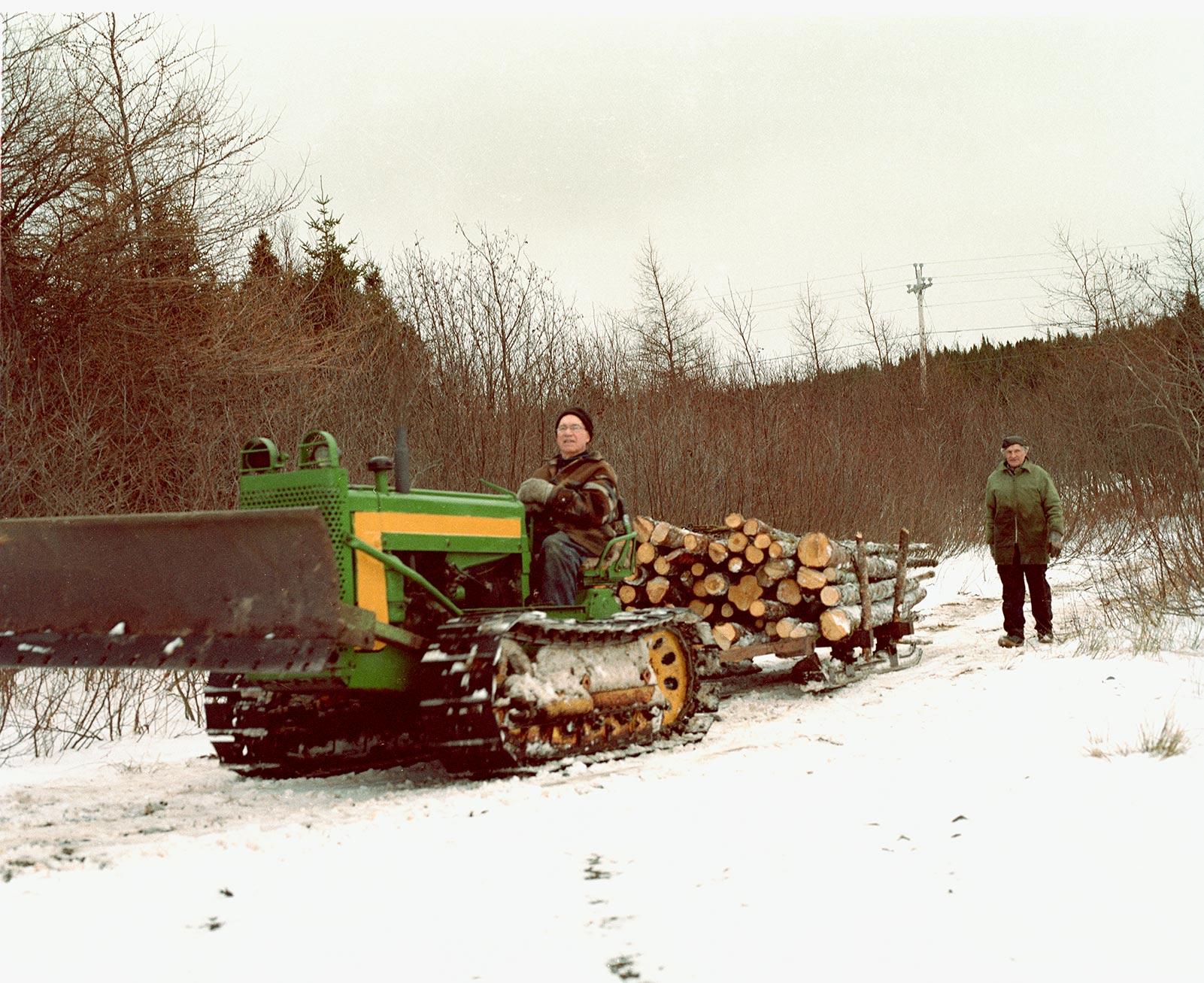 my father and his brother hauling wood logs with an old John Deere tractor